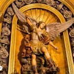 Escultura de San Miguel Arcángel en una iglesia, representado con armadura y espada en alto, simbolizando la protección y la lucha contra el mal.