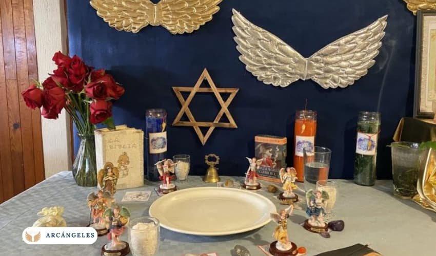 Altar dedicado a los 7 arcángeles con velas, estatuillas, rosas y símbolos espirituales, incluyendo un Estrella de David y alas doradas en el fondo.