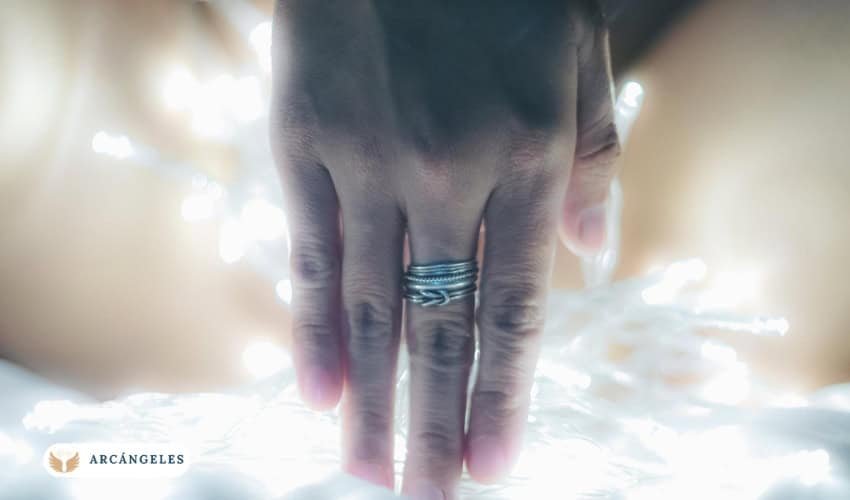 Mano con un anillo inspirado en San Miguel Arcángel, rodeada de luz, simbolizando protección espiritual y conexión divina.