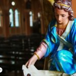 Imagen de una estatua de un arcángel en una iglesia, simbolizando la presencia divina y la protección espiritual. El arcángel está vestido con ropas celestiales de tonos azules y dorados, y sostiene un pergamino en sus manos, representando la transmisión de bendiciones y mensajes divinos.