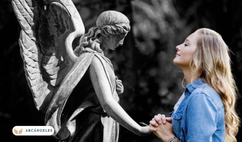Mujer en oración frente a una estatua de ángel, simbolizando la conexión espiritual con el Arcángel Uriel para atraer abundancia y prosperidad.
