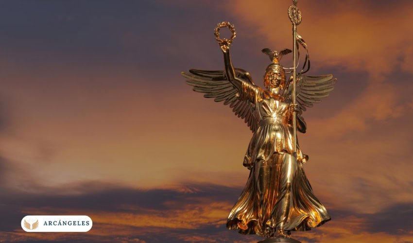 Estatua dorada de un arcángel al atardecer, sosteniendo una corona y un bastón, representando la protección y guía divina.