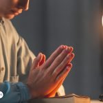 Persona rezando en un espacio tranquilo con las manos juntas y una Biblia abierta, simbolizando un momento de oración y reflexión espiritual.