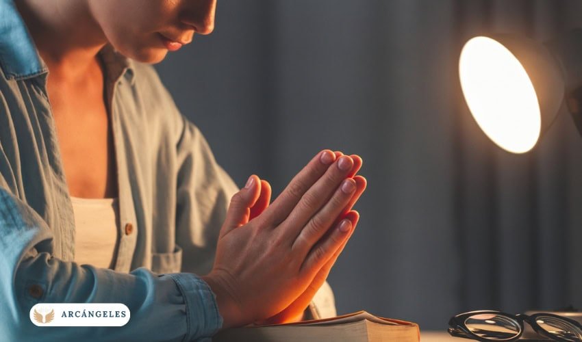 Persona rezando en un espacio tranquilo con las manos juntas y una Biblia abierta, simbolizando un momento de oración y reflexión espiritual.