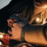 Manos entrelazadas de una pareja iluminadas por luces cálidas, representando conexión, amor y devoción espiritual en el contexto de la novena al Arcángel para el amor