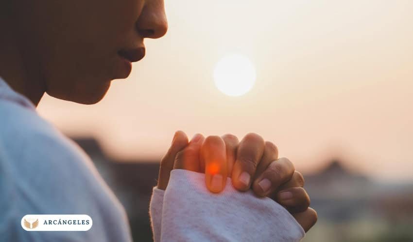 Persona orando con las manos juntas al amanecer, simbolizando fe y conexión espiritual en momentos de búsqueda de salud y protección divina.