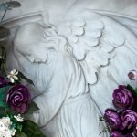 Imagen de un relieve de San Miguel Arcángel rodeado de flores moradas y rojas, símbolo de ofrendas y devoción espiritual.