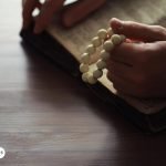 Persona sosteniendo un rosario blanco mientras reza con una Biblia abierta, simbolizando la devoción y conexión espiritual con los arcángeles.