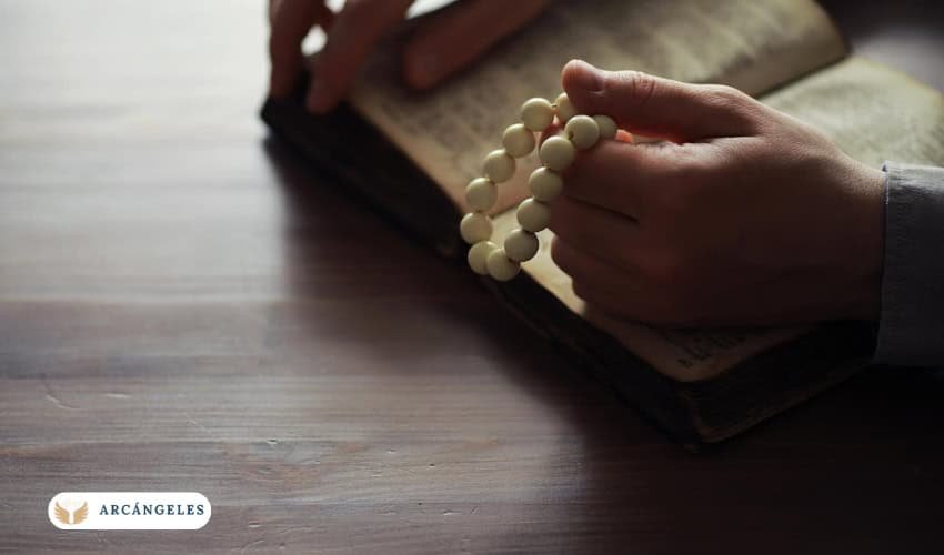 Persona sosteniendo un rosario blanco mientras reza con una Biblia abierta, simbolizando la devoción y conexión espiritual con los arcángeles.